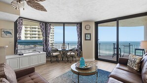 Un soggiorno con vista sull'oceano, un balcone con ringhiera e un'area pranzo con tavolo e sedie.