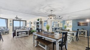 Un'ampia sala da pranzo con un tavolo e panche in legno, una cucina sullo sfondo e una ventola a soffitto.