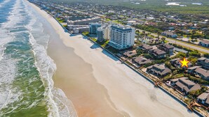 Vue aérienne d’une ville côtière avec une plage, des immeubles résidentiels et un hôtel offrant une vue sur l’océan.