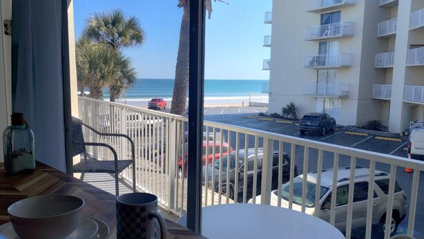 Un balcone con vista sulla spiaggia, auto parcheggiate e un edificio con balconi.