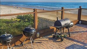 Un balcone con vista sulla spiaggia e sull'oceano, dotato di due barbecue portatili.