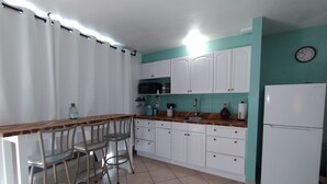 Una cucina con mobili bianchi, un piano di lavoro in legno, un lavello, un frigorifero e una sveglia appesa al muro.