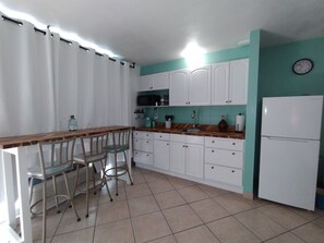 A kitchen with white cabinets, a wooden countertop, a sink, a refrigerator, and a clock on the wall. - Ocean Front Studio (Daytona Beach)