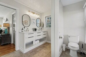 Un baño moderno con un tocador blanco, dos espejos grandes, un inodoro y una ventana con persianas.