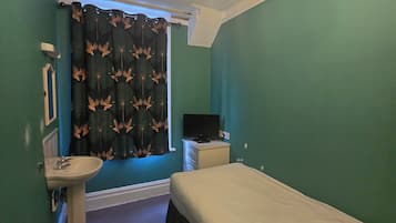 A bedroom with a bed, a bedside table, a television, and a window with curtains.