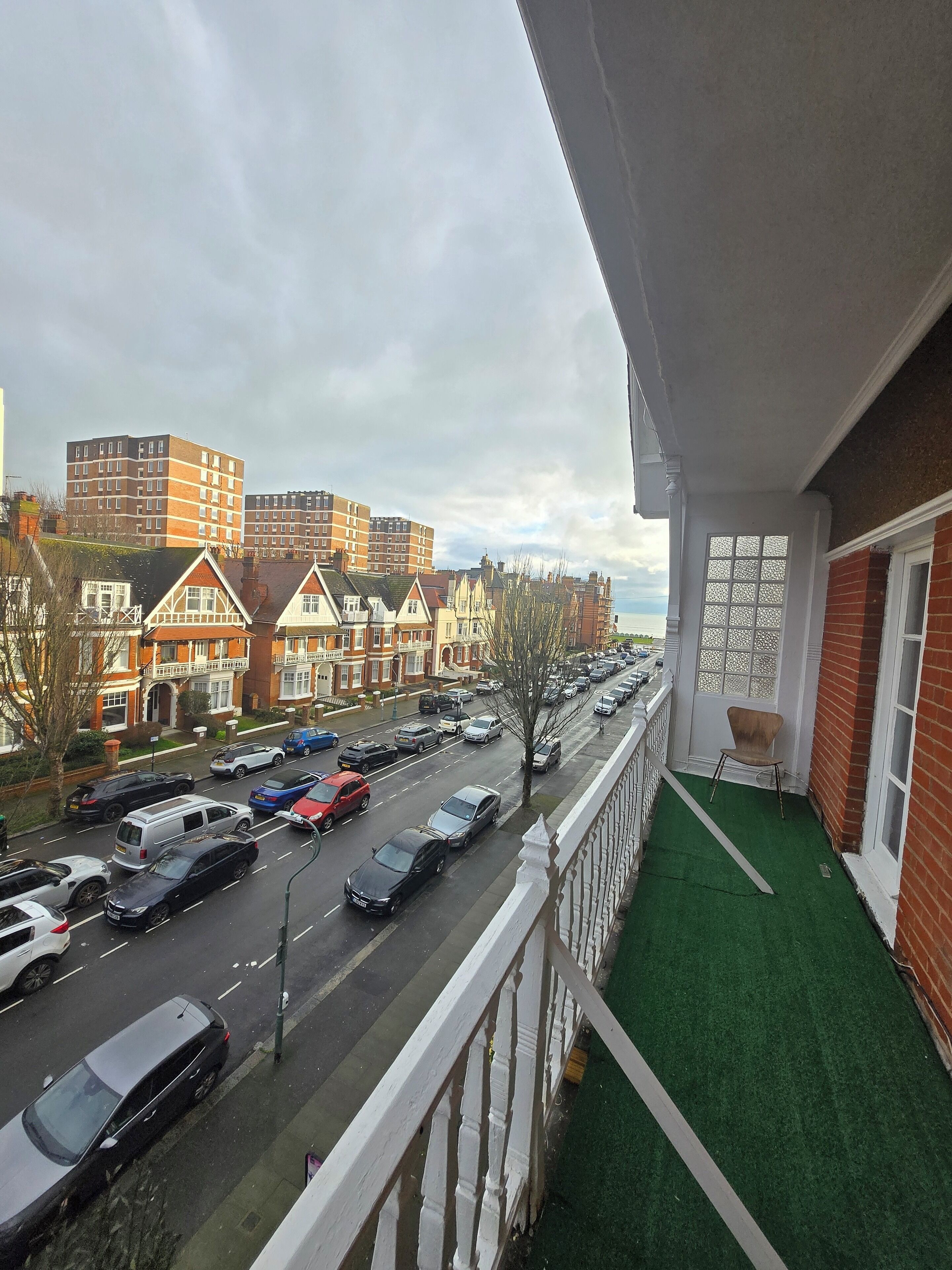 Un balcon donnant sur une rue bordée de voitures garées et d’immeubles d’habitation.
