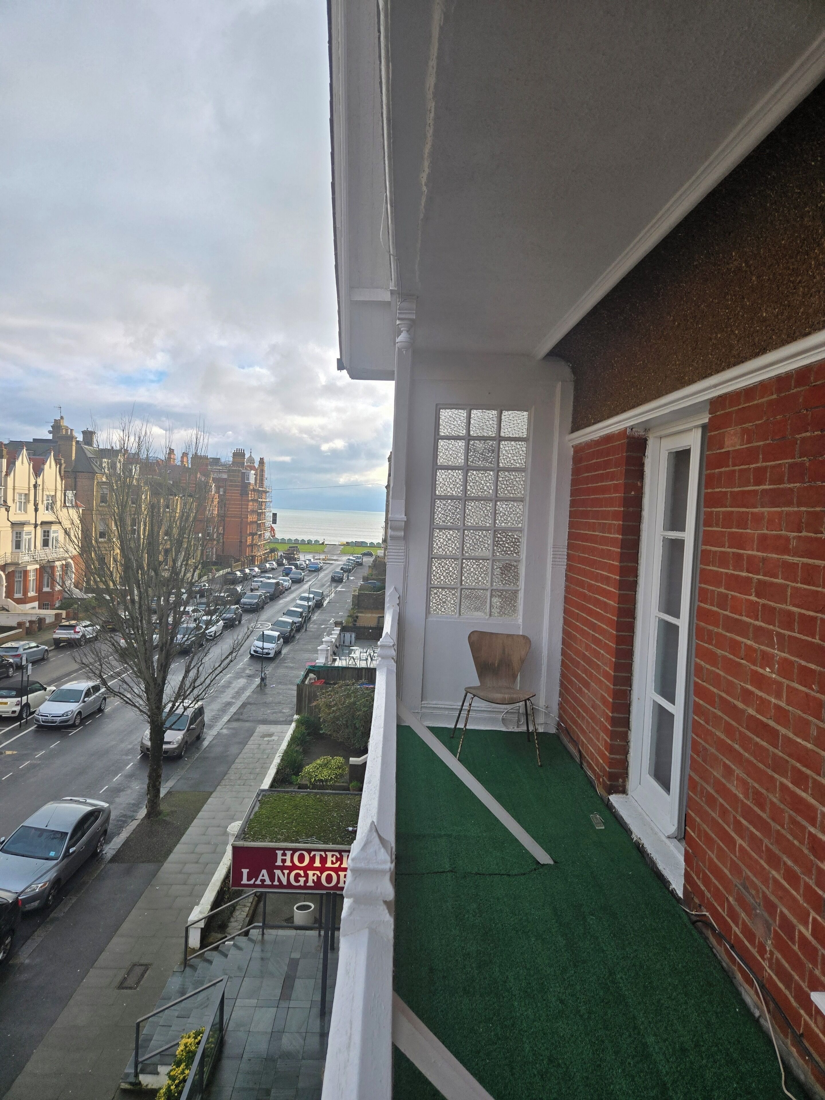 A balcony with a view of a city street, a chair, and a sign for a hotel.
