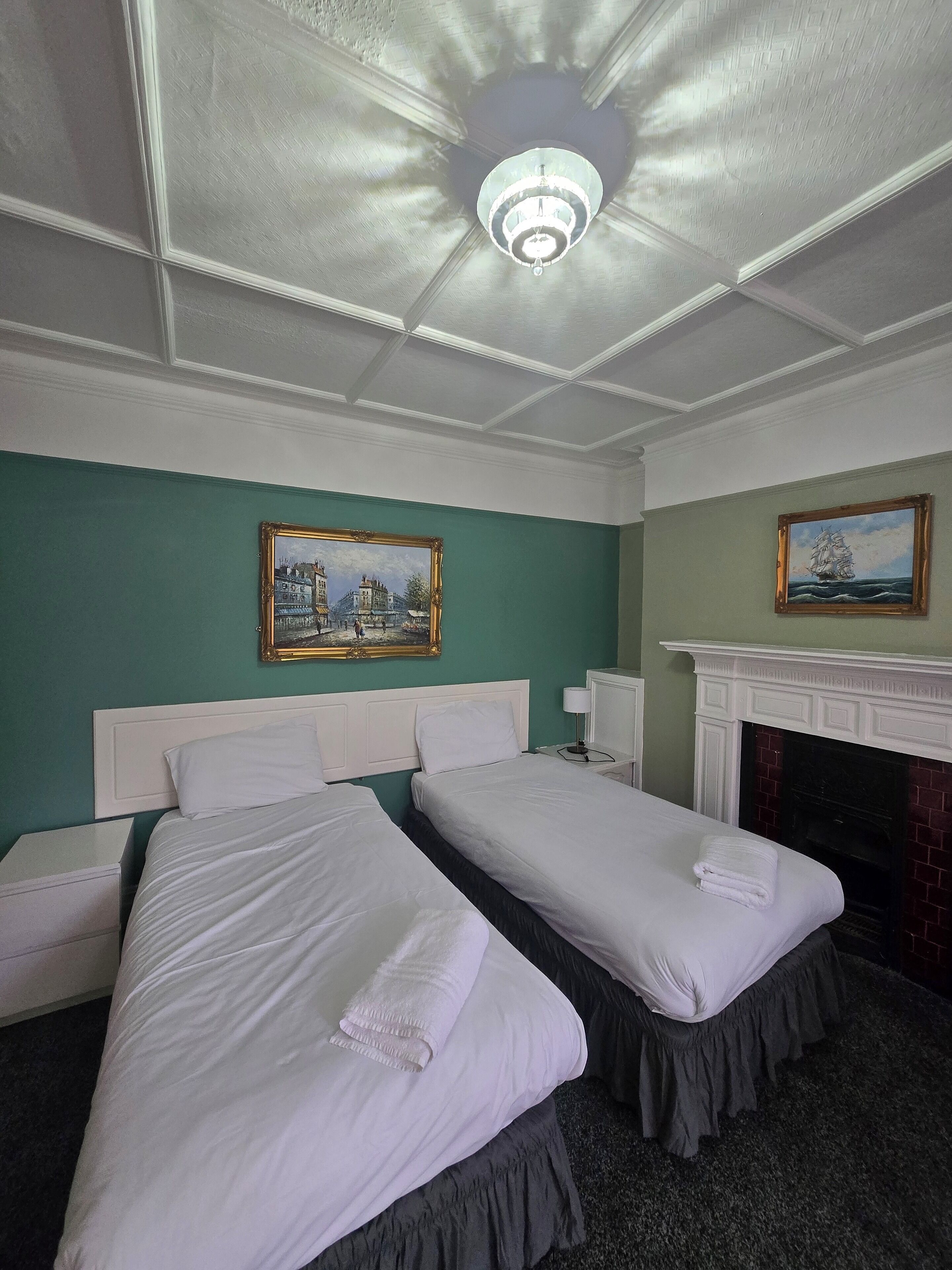 Une chambre d’hôtel avec deux lits simples, une cheminée et deux tableaux accrochés aux murs.