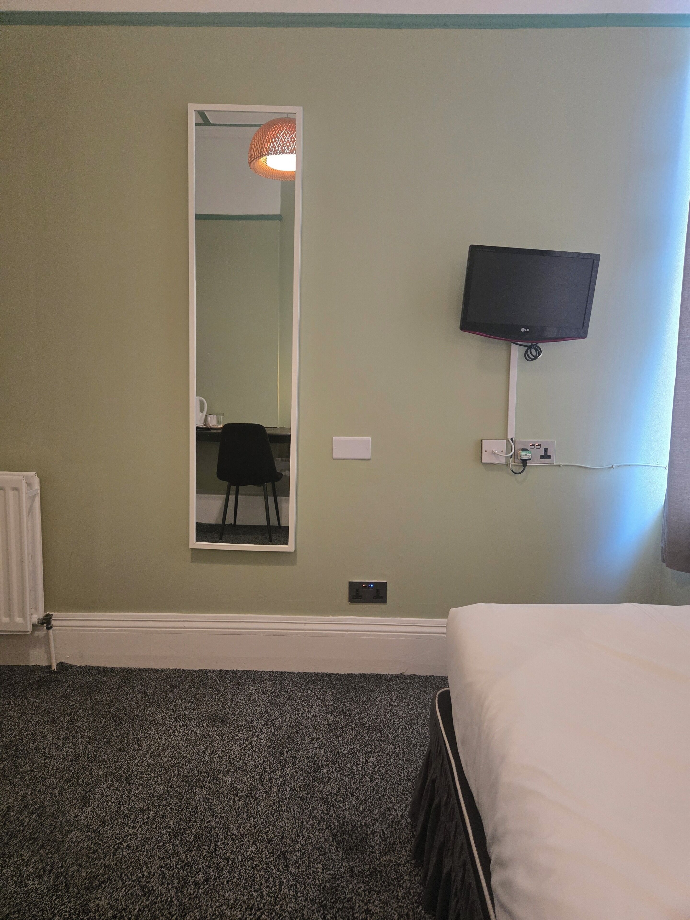 A hotel room with a bed, a television mounted on the wall, a mirror, and a radiator.