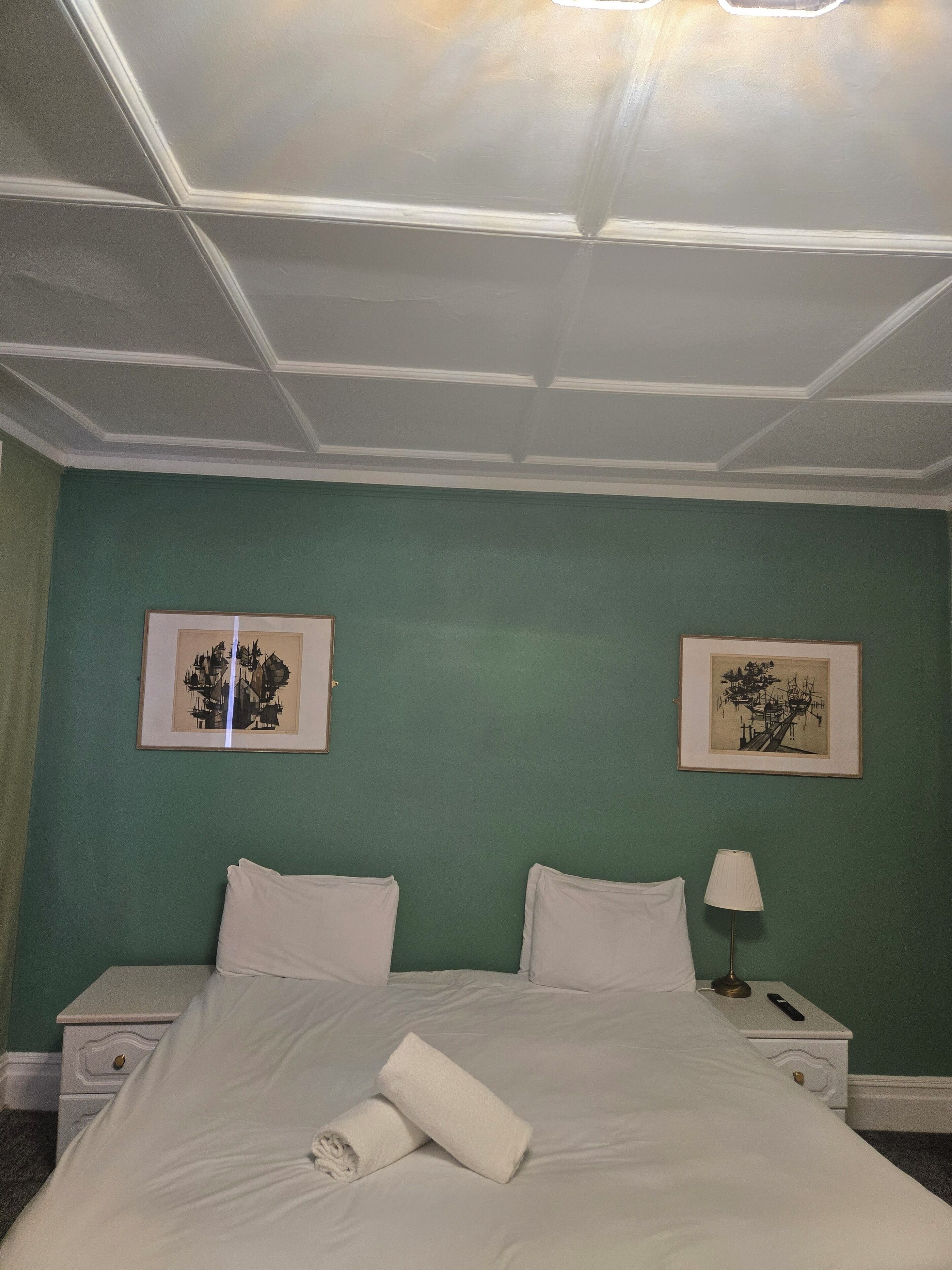Hotelkamer met een bed, twee nachtkastjes, een lamp en twee ingelijste foto’s aan de muur.