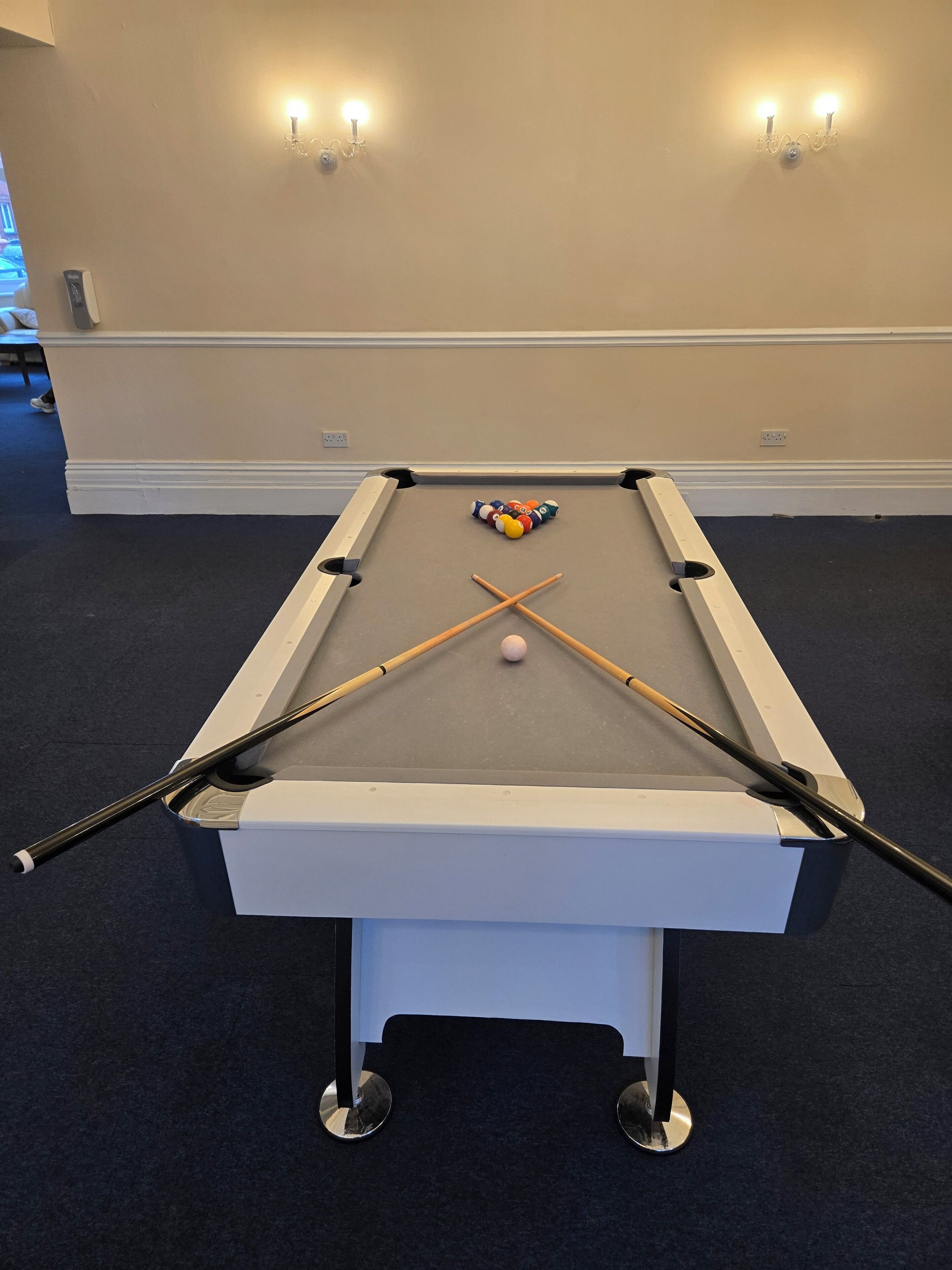 A pool table with a white cloth, two pool cues, and a cue ball.