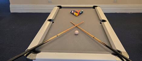 A pool table with a white cloth, two pool cues, and a cue ball.