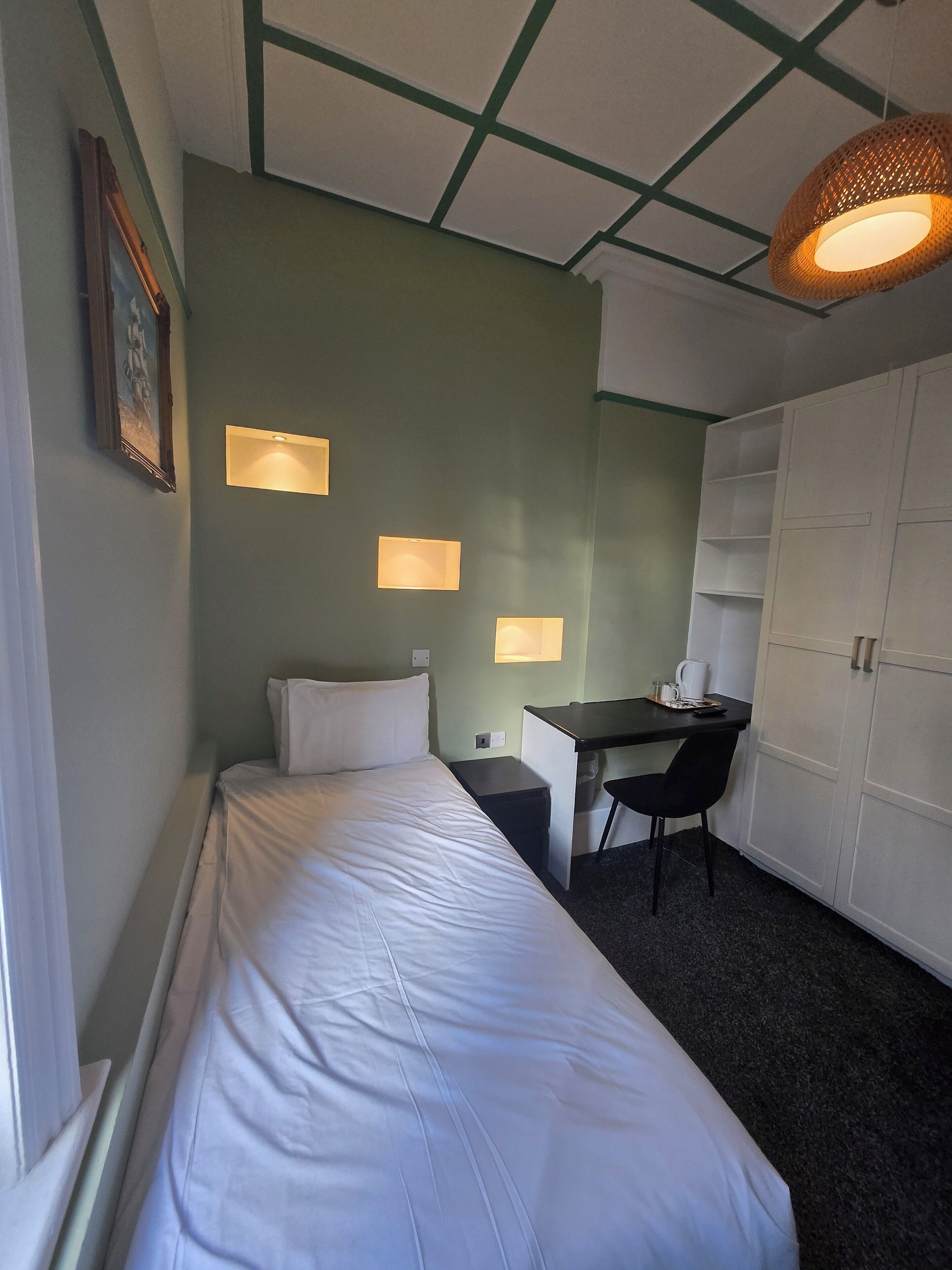 Camera d'albergo con letto, scrivania, sedia, armadio e luci a parete.