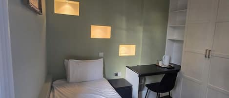 A hotel room with a bed, desk, chair, wardrobe, and wall-mounted lights.