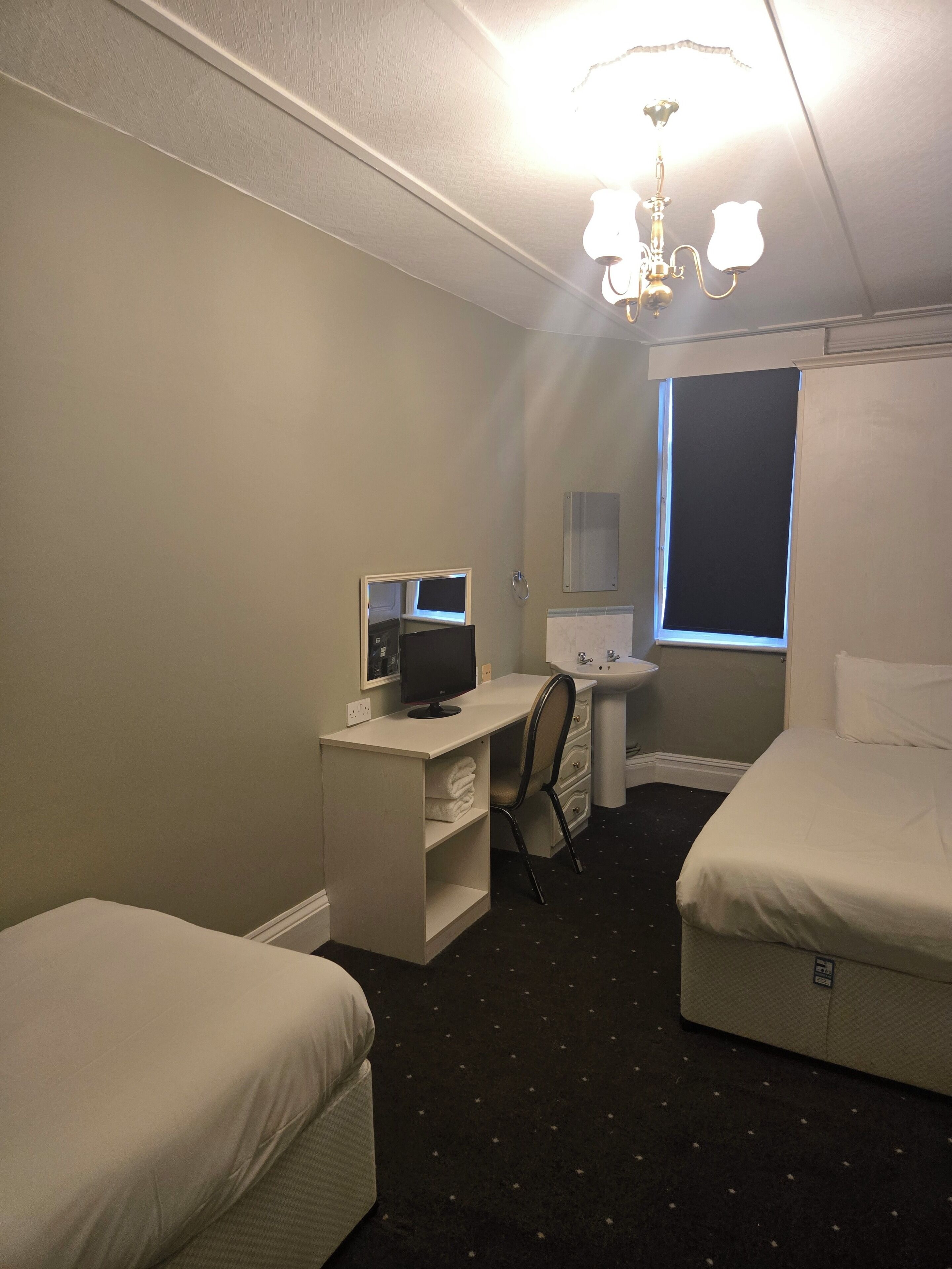 Camera d'albergo con due letti, una scrivania con un computer, una sedia, un piccolo tavolo con una lampada e una finestra.