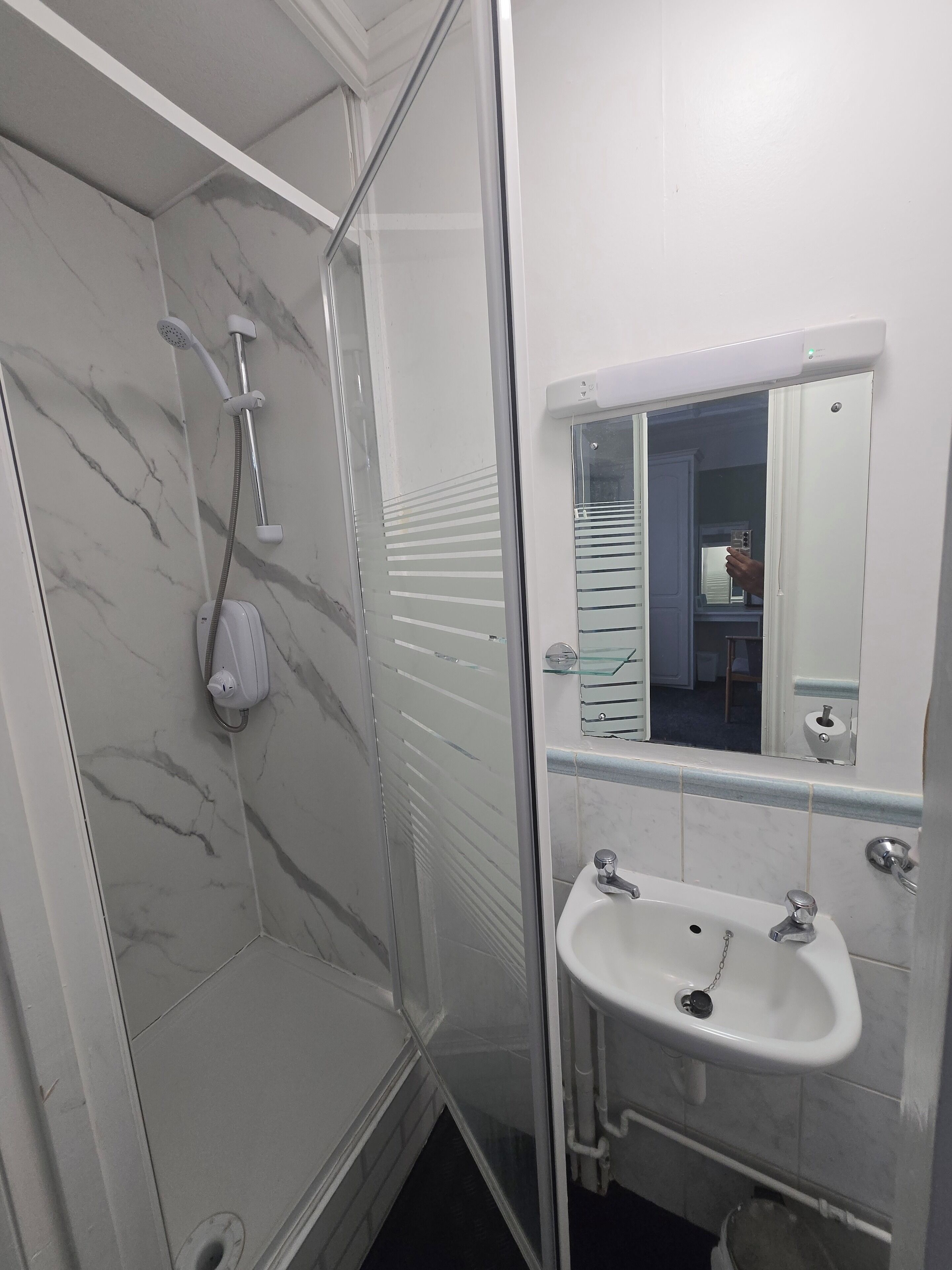 A bathroom with a glass-enclosed shower, a white sink, and a mirror above it.