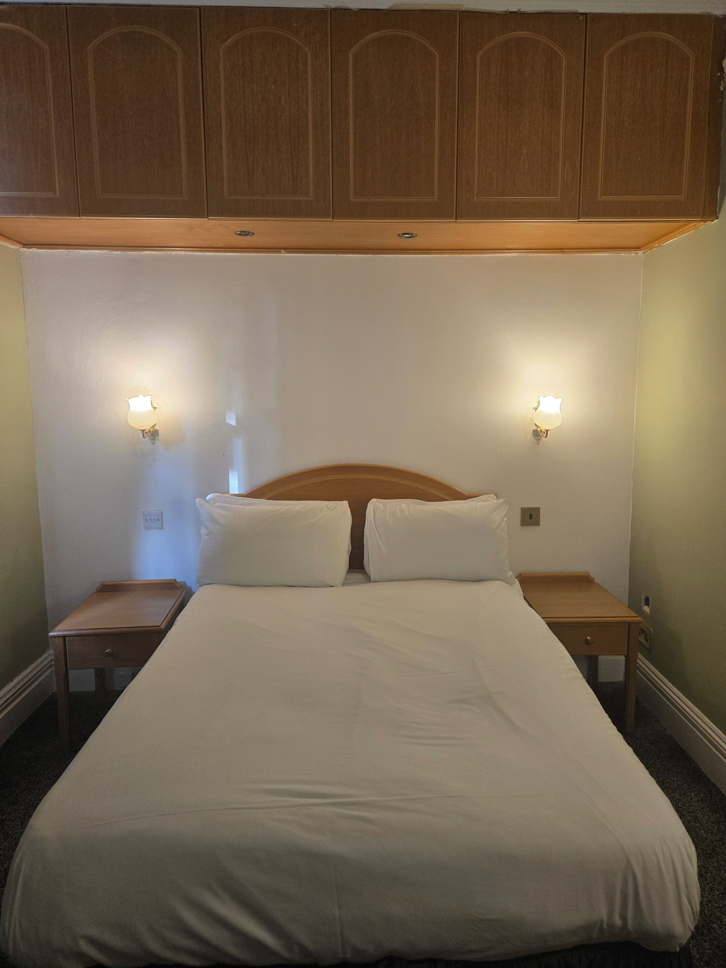 Ein Schlafzimmer mit einem großen Bett, zwei Nachttischen, einem Holz-Kopfteil und wandmontierten Leuchten.