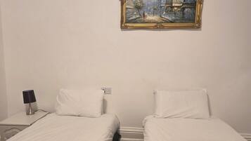 A hotel room with two single beds, a nightstand with a lamp, and a painting on the wall.