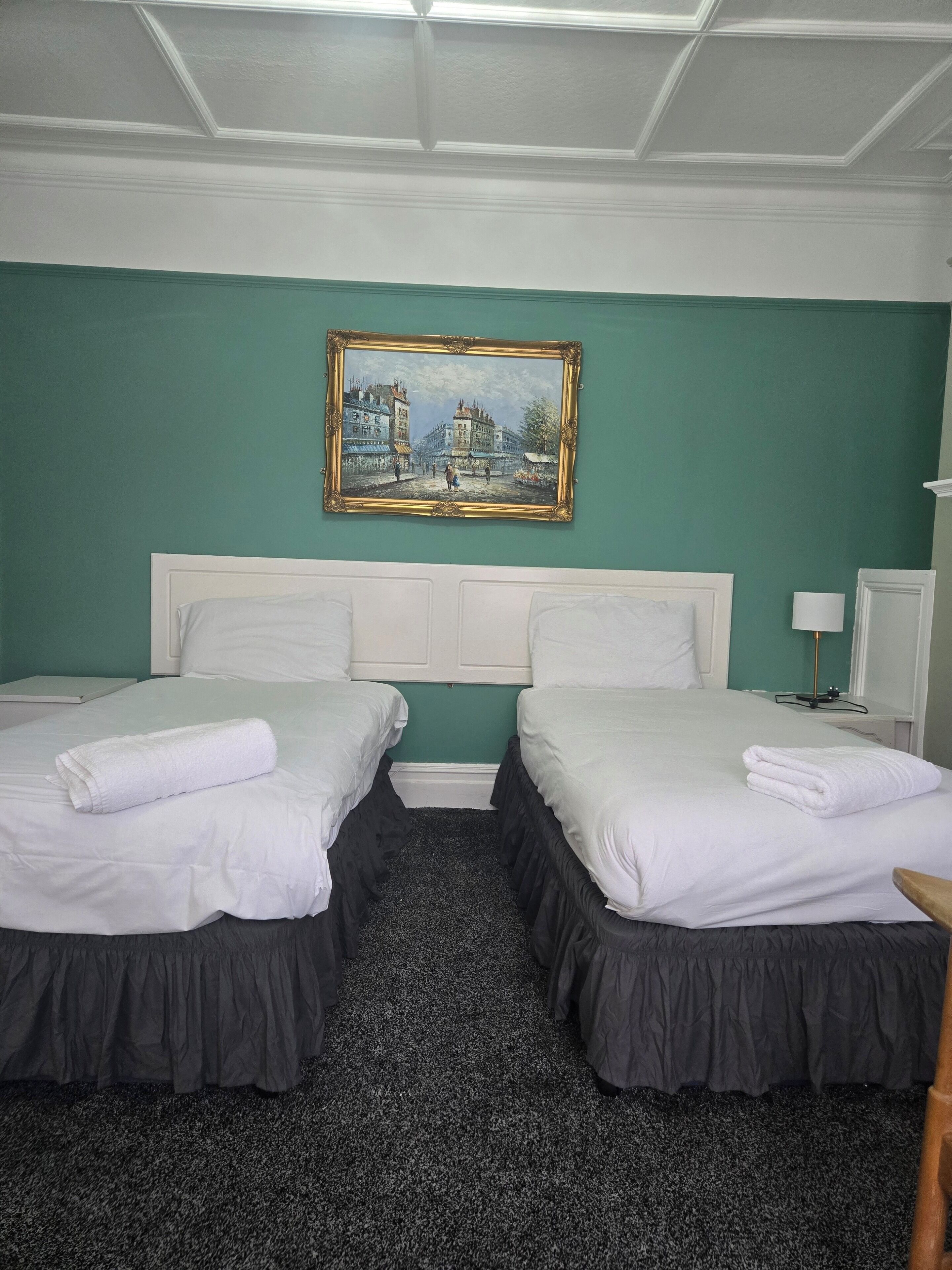 Une chambre d’hôtel avec deux lits, un tableau au mur et une petite table avec une lampe.