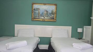 Une chambre d’hôtel avec deux lits, un tableau au mur et une petite table avec une lampe.