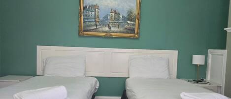 A hotel room with two beds, a painting on the wall, and a small table with a lamp.