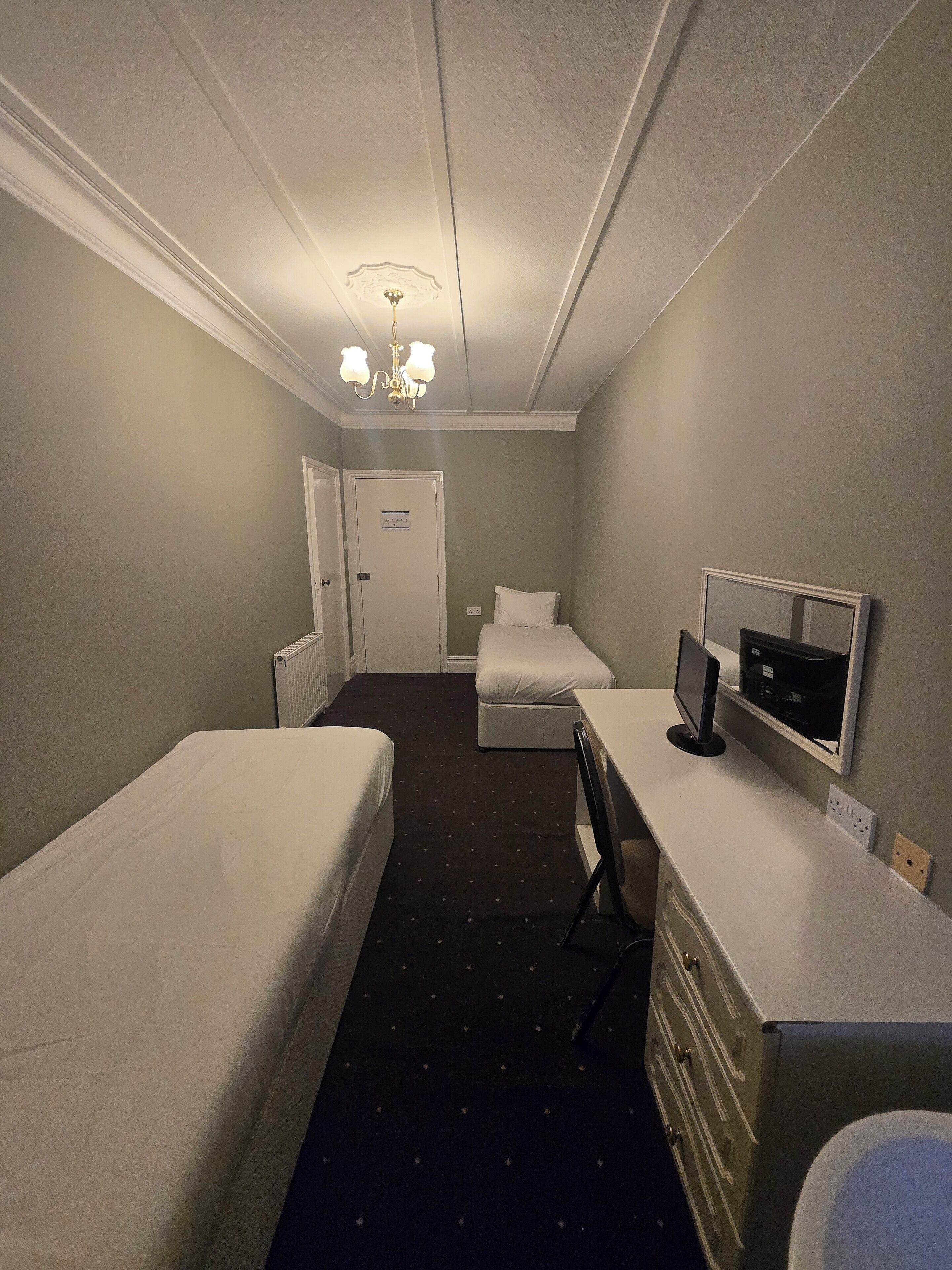 A hotel room with two single beds, a desk with a computer, a chair, and a TV.