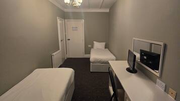 Habitación de hotel con dos camas individuales, un escritorio con computadora, una silla y un televisor.