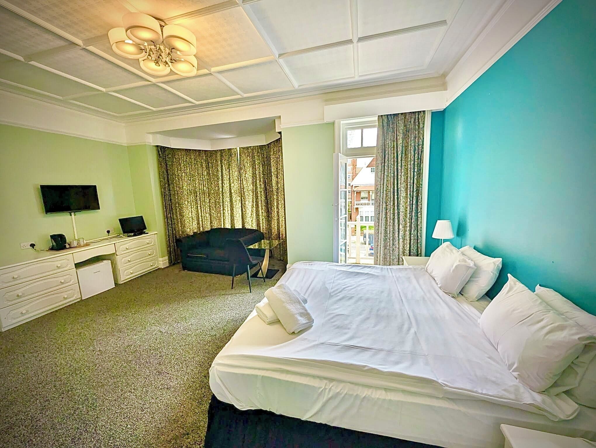 A hotel room with a bed, a TV, a desk, a chair, and a view of buildings through a window.