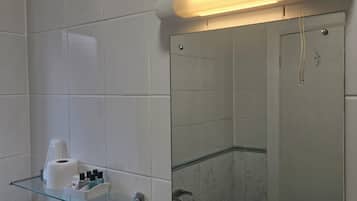 A bathroom with a toilet, a glass shelf with toiletries, a mirror, and a light fixture.