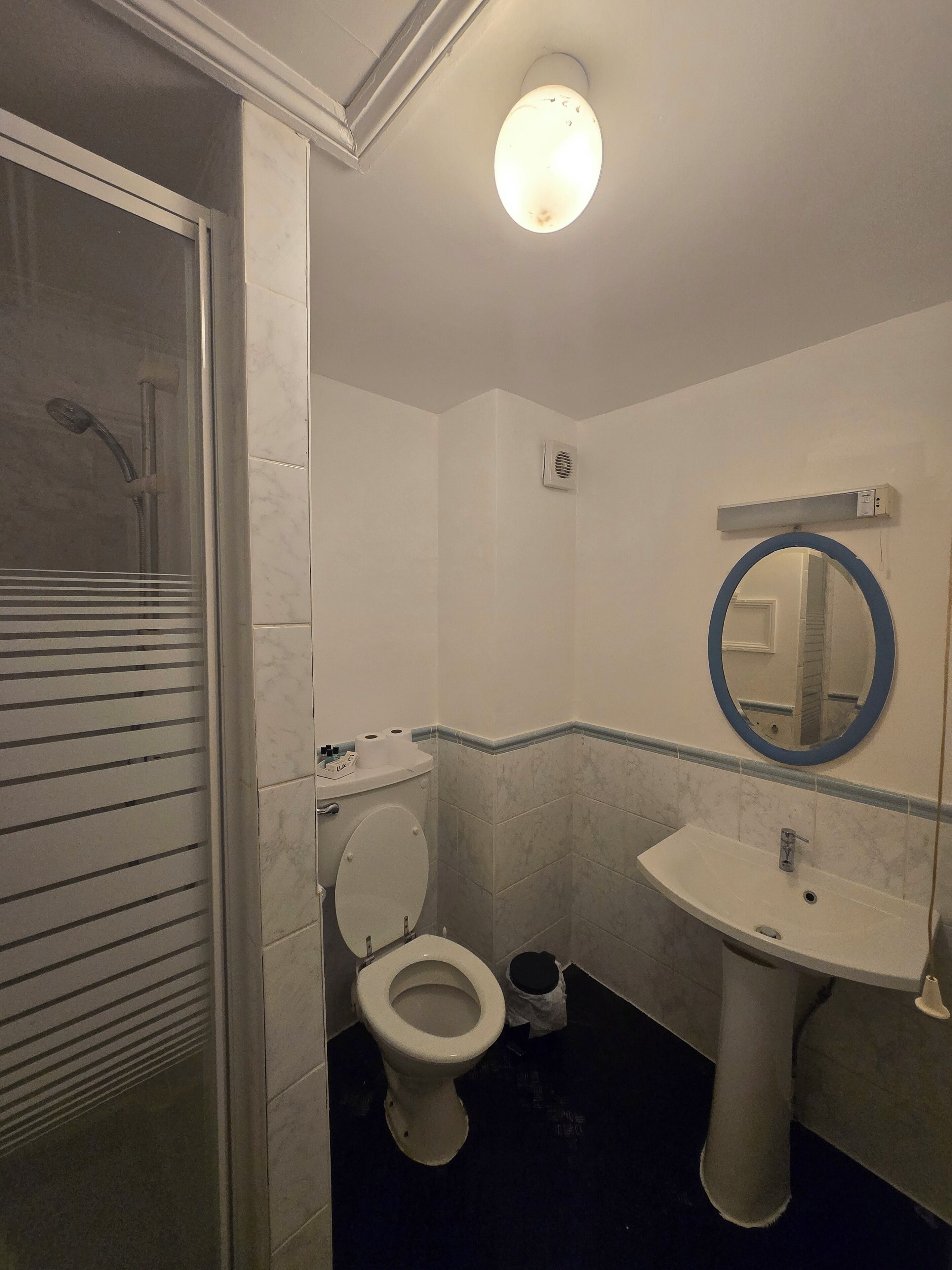 Une salle de bain équipée de toilettes, d’un lavabo, d’un miroir, d’une douche et d’une poubelle.