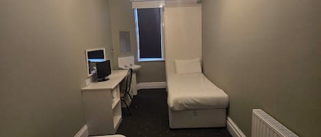 A hotel room with two single beds, a desk with a computer, a window, and a radiator.
