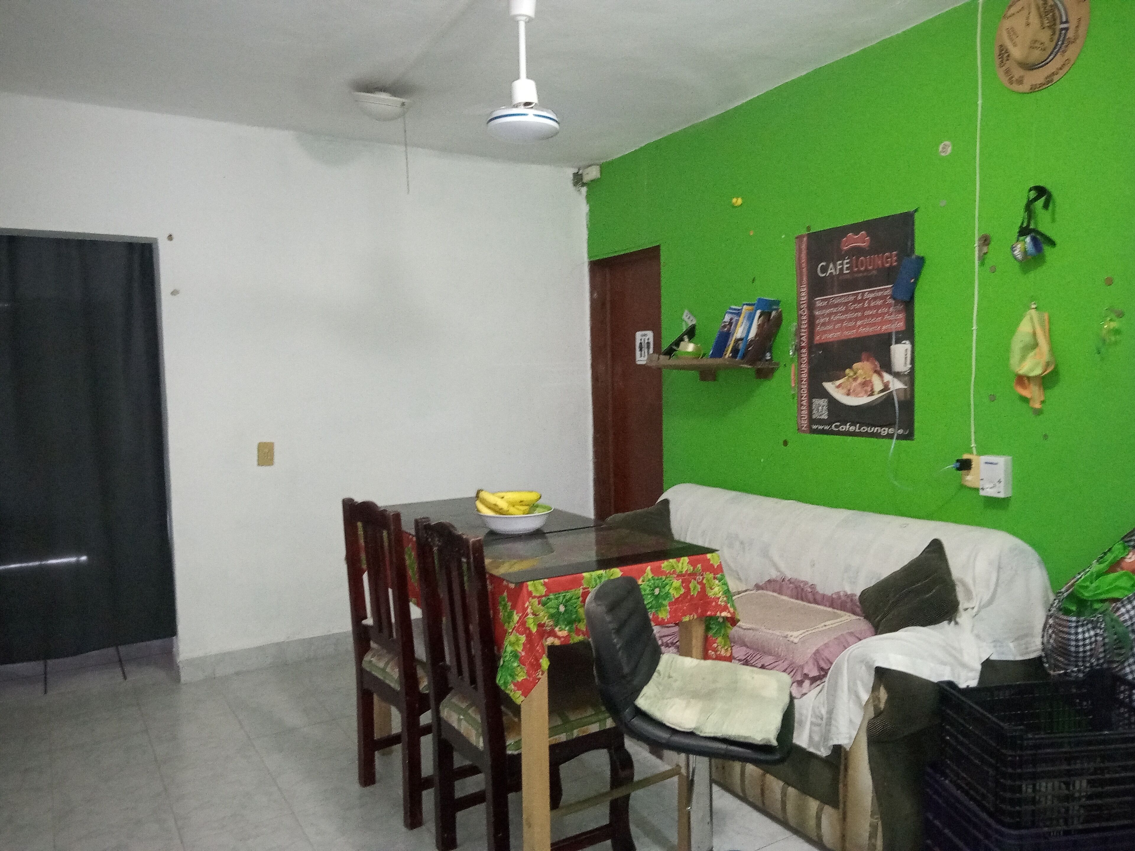 A dining area with a table, chairs, a bowl of fruit, and a green wall with a poster.