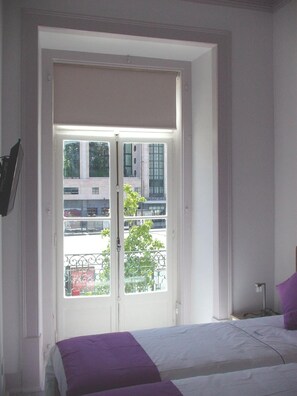 A room with a bed, a window with a view of buildings, and a door. - 'Inn Chiado - Double Room 1' with Balcony, Wi-Fi and Air Conditioning (Lisboa)