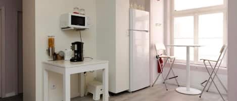 Una kitchenette pequeña con microondas, cafetera y refrigerador. Se ve una ventana con vistas al exterior.