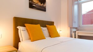 A hotel room with a bed, two pillows, a nightstand, a wall-mounted picture, and a window. - Double Room 5 at Inn Chiado with Wi-Fi and Air Conditioning (Lisboa)