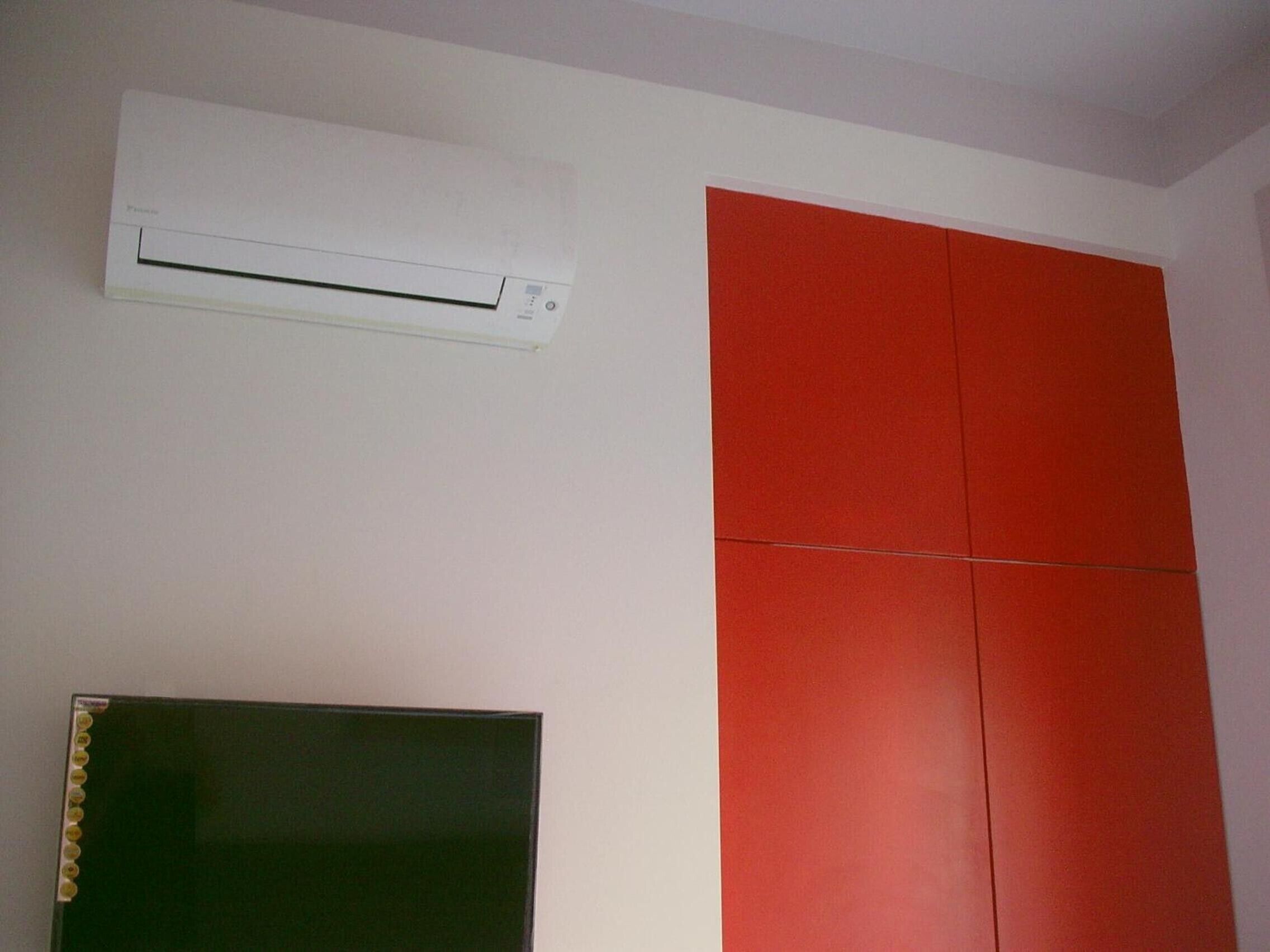 Ein Zimmer mit weißer Wand, roter Trennwand und einem Flachbildfernseher.