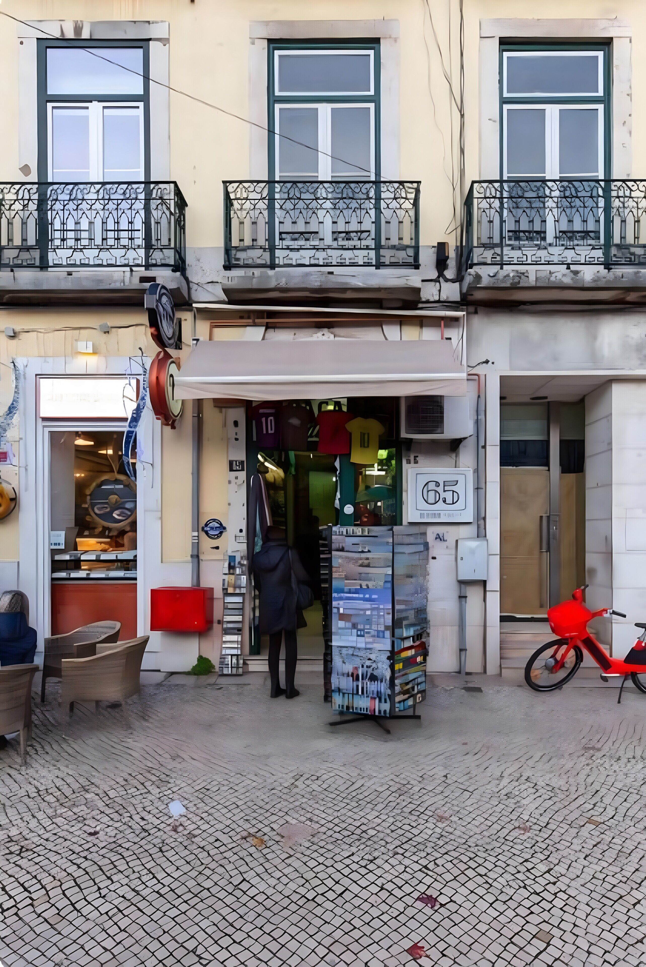 A building with a shop entrance, a red scooter, and a sign with the number 65.