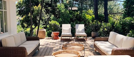 An outdoor seating area with wicker furniture and a white sofa, surrounded by trees and a clear sky.