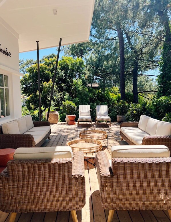 An outdoor seating area with wicker furniture and a white sofa, surrounded by trees and a clear sky. - Renovated house in top Cap Ferret location A0344 (Lège-Cap-Ferret)
