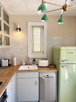 Una cocina con un refrigerador verde, un lavamanos blanco, un tostador y una ventana con vistas.