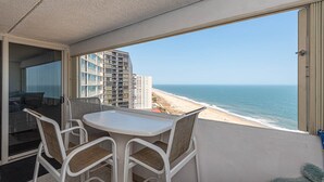 A balcony with a table and chairs, overlooking a beach and ocean. - Oceanfront 15th Floor Condo w/ Balcony & Pool (Ocean City)