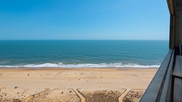 A beach view from a window overlooking a sandy beach with a clear sky. - Oceanfront 15th Floor Condo w/ Balcony & Pool (Ocean City)