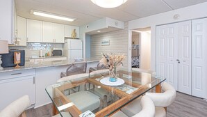 A modern kitchen with white cabinets, a glass dining table, and a ceiling light fixture. - Oceanfront 15th Floor Condo w/ Balcony & Pool (Ocean City)