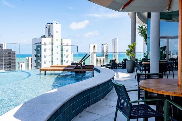 A rooftop pool with a view of the ocean and city skyline, surrounded by outdoor seating and a large planter. - Luxury Apartment in the Building. Gameleira Beach, Boa Viagem 1608 (Recife)