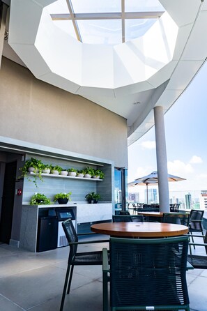 A modern outdoor seating area with a round table and chairs, a vending machine, and potted plants on shelves. - Luxury Apartment in the Building. Gameleira Beach, Boa Viagem 1608 (Recife)