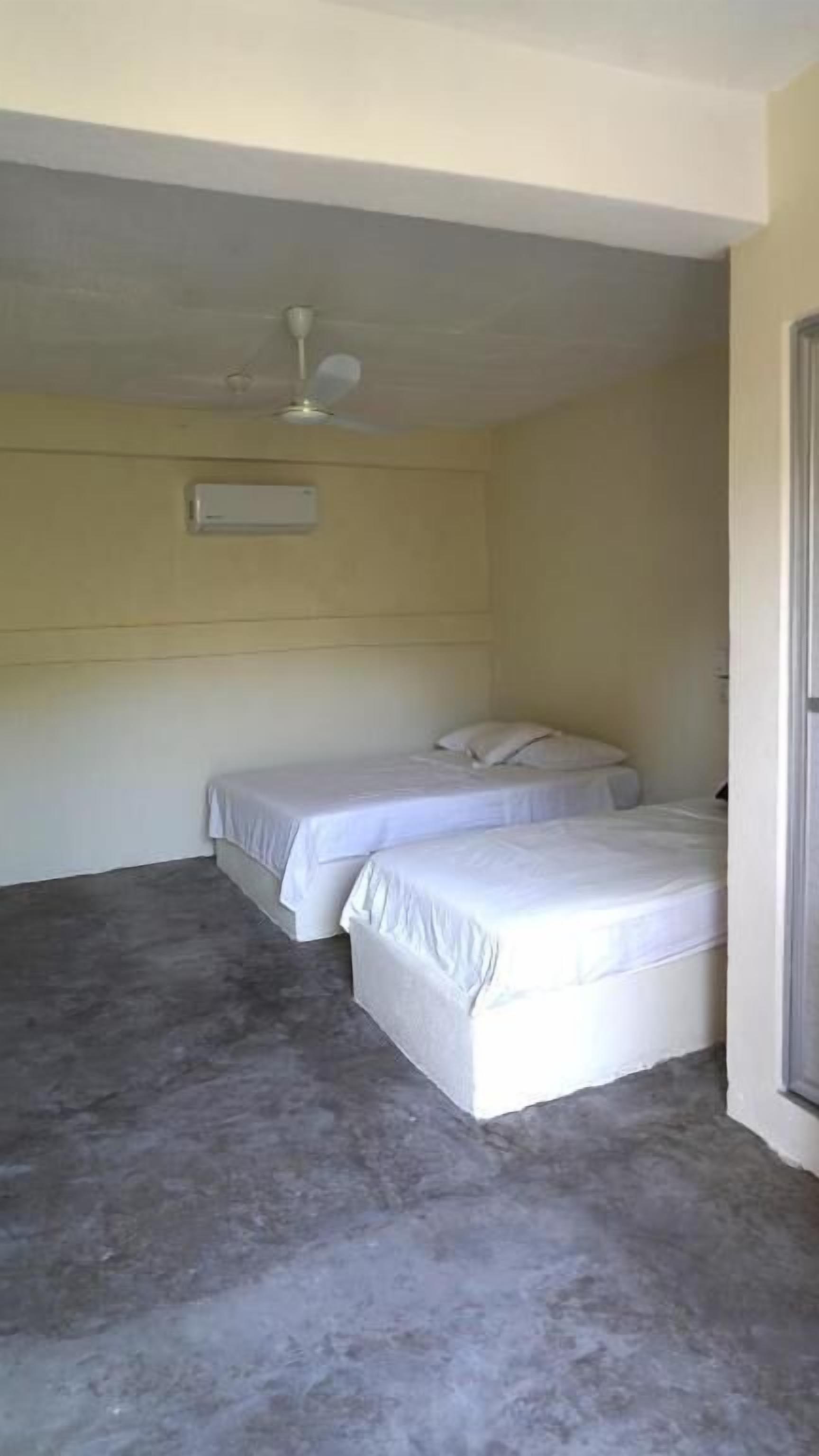 A room with two single beds, a ceiling fan, and a light switch on the wall.