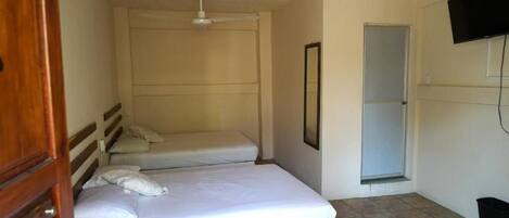 A small, clean room with two single beds, a ceiling fan, a window, and a TV mounted on the wall.