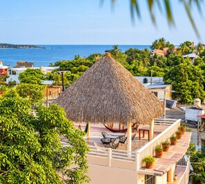 A thatched-roof gazebo with outdoor seating, surrounded by lush greenery and overlooking a coastal area. - Casa Laani (San Pedro Mixtepec)