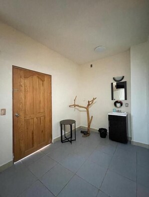 A room with a wooden door, a small round table, a coat rack, a black cabinet with a mirror, and a tiled floor. - Casa Laani (San Pedro Mixtepec)