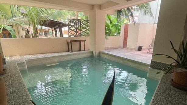 A swimming pool with a tiled edge, surrounded by a covered patio area with chairs and a table. - Casa Laani (San Pedro Mixtepec)
